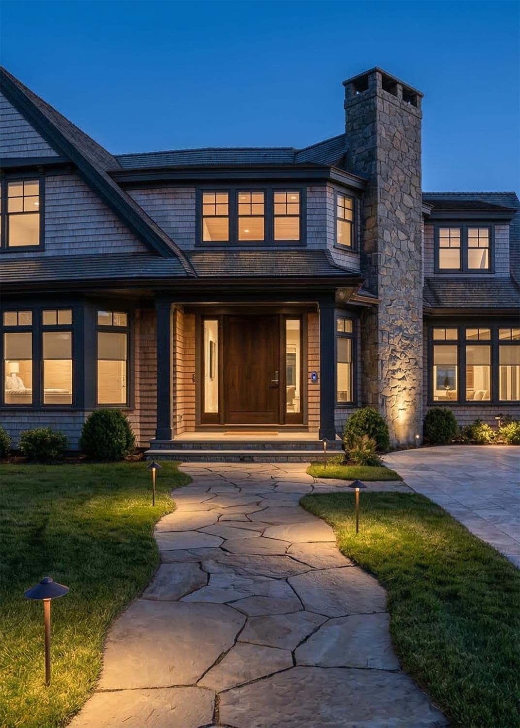 Stone walkway illuminated by landscape lights leading to a two-story home entrance at dusk
